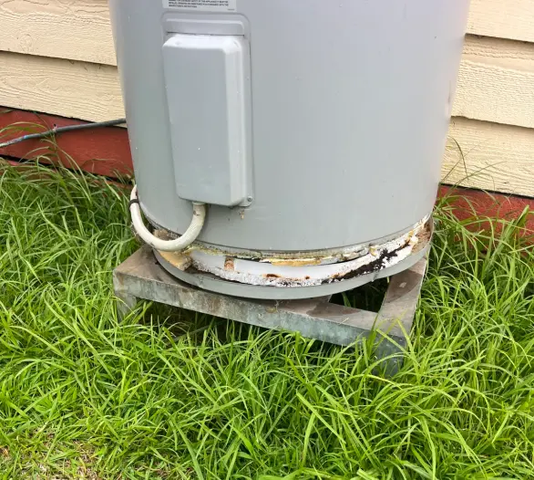 Base of a hot water unit sitting on a steel stand in long grass