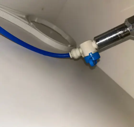 Blue push-fit water line and filter housing wrench inside a cabinet