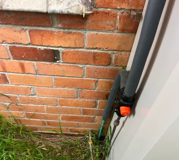 Bottom of a gas hot water unit with a gas label and pipes above grass