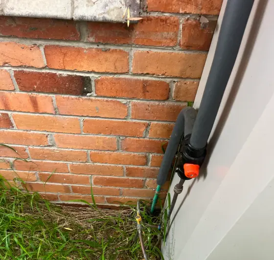 Bottom of a gas hot water unit with a gas label and pipes above grass