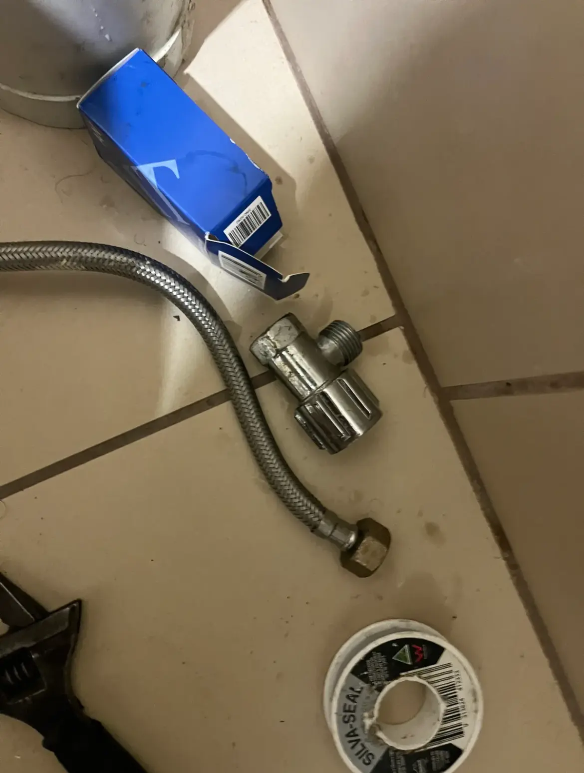 Braided flexible hose, an angle stop, thread tape and spanner on a tiled floor