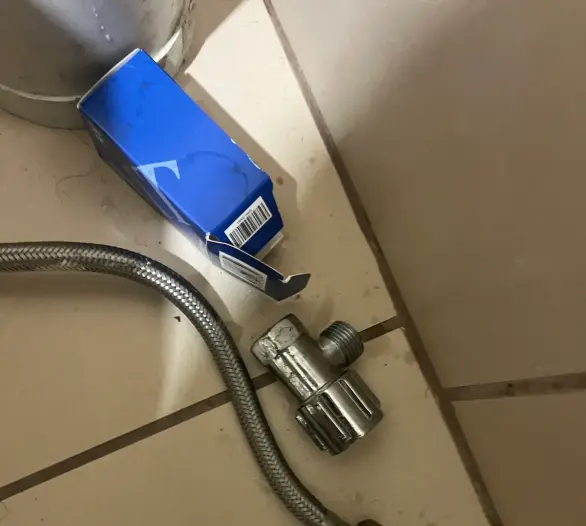 Braided flexible hose, an angle stop, thread tape and spanner on a tiled floor