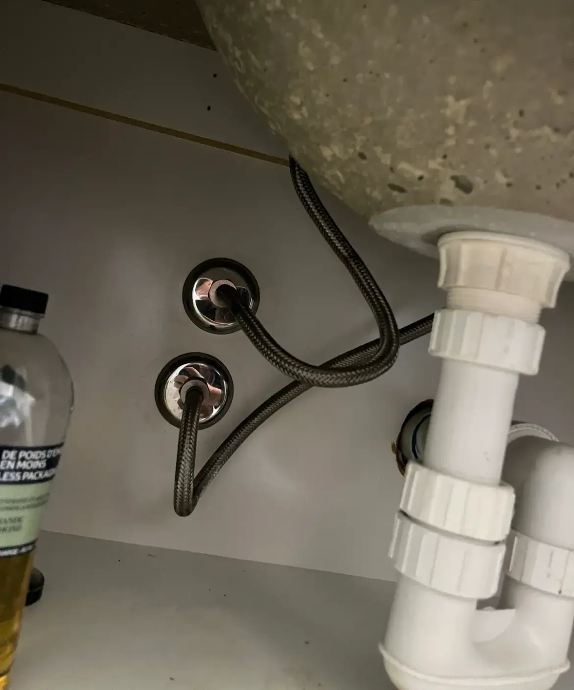 Braided flexible hoses and a plastic trap under a basin in a vanity cupboard