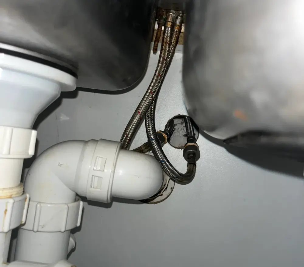 Braided hoses and a plastic trap under a sink inside a cupboard