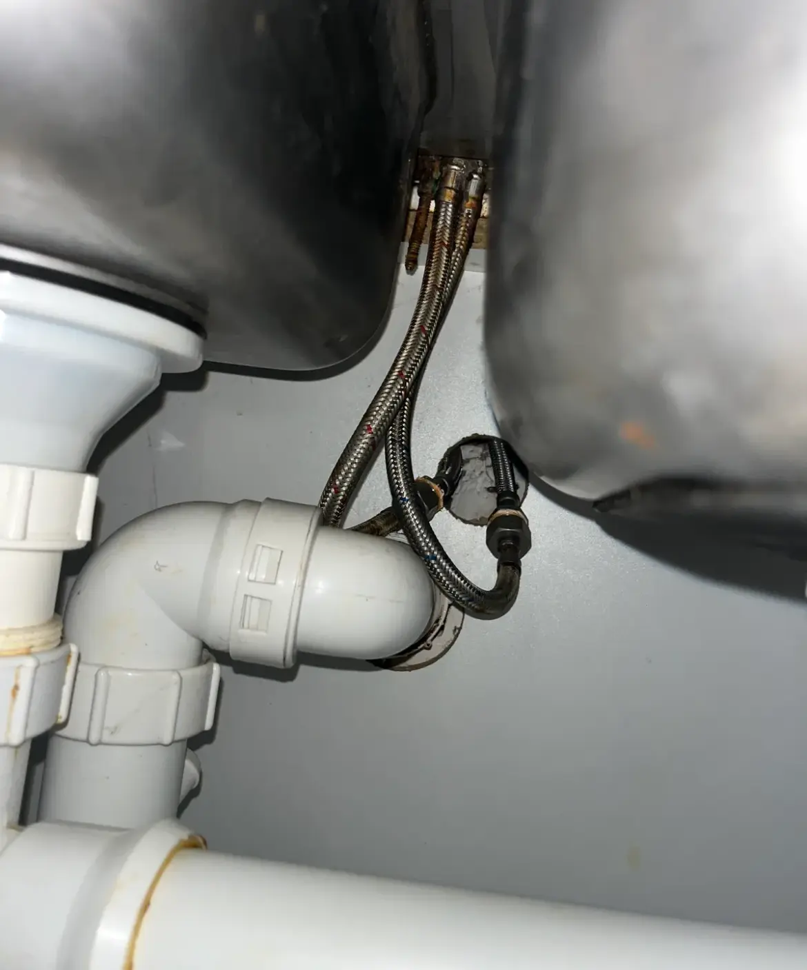 Braided hoses and a plastic trap under a sink inside a cupboard