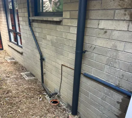 Brick wall with a downpipe, drain and copper pipe running to the ground