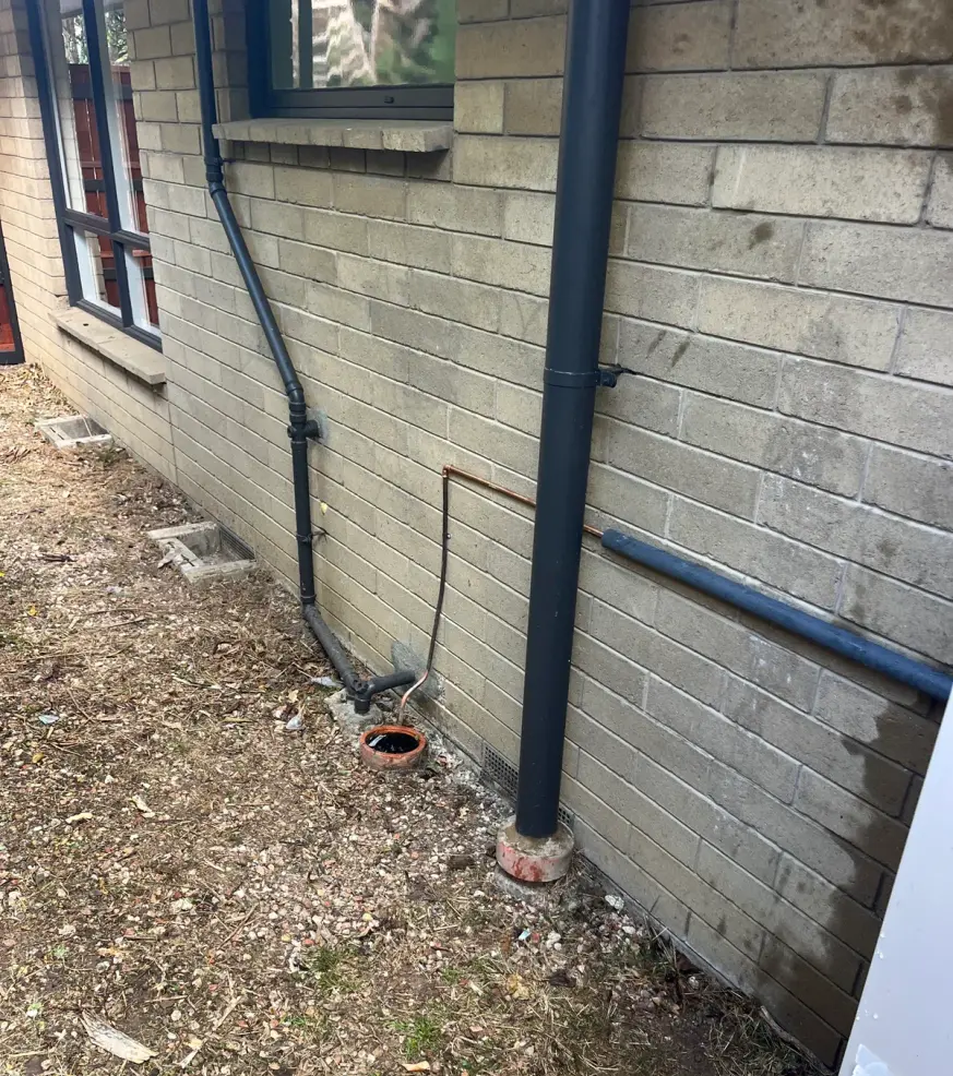 Brick wall with a downpipe, drain and copper pipe running to the ground