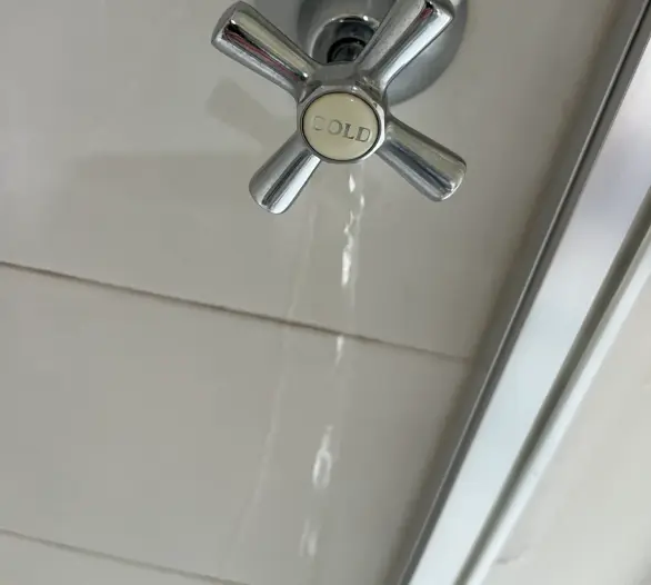 Chrome cross-handle shower tap with water running down the tiles
