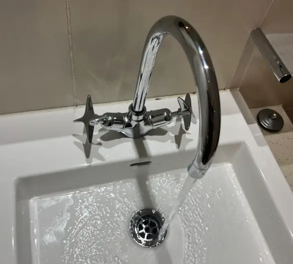 Chrome gooseneck tap with cross handles running water into a white basin