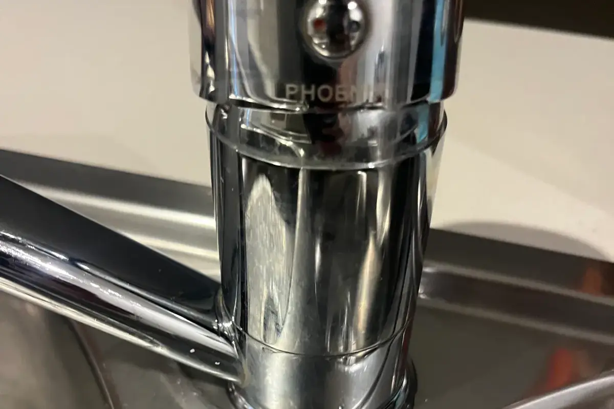 Close-up of a chrome mixer tap base on a stainless steel double sink