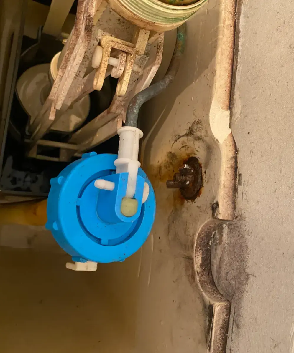 Close view inside a toilet cistern showing a blue fill valve and a rusty bolt