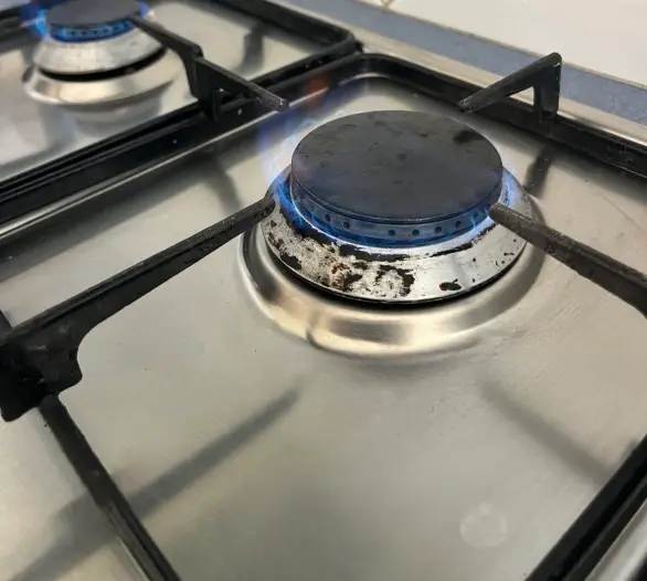 Close view of a lit gas burner on a cooktop with a blue flame