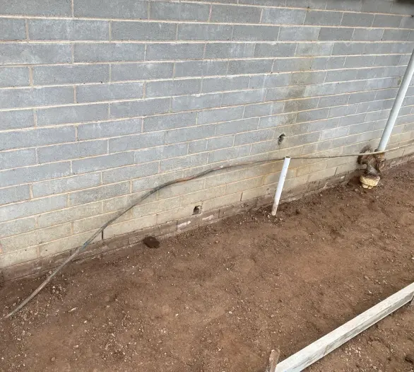 Close view of pipework in a trench beside a block wall