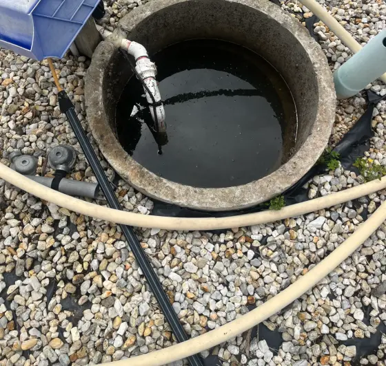 Concrete pit with pump housing, hoses and a gravel surround