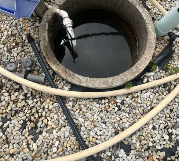 Concrete pit with pump housing, hoses and a gravel surround