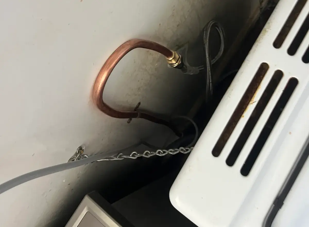 Copper gas bayonet fitting and chain behind an appliance