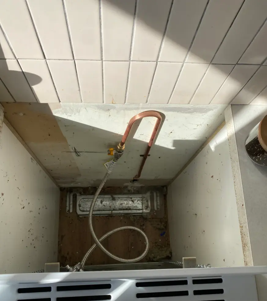 Copper gas pipe and braided hose in a cupboard above a tiled floor