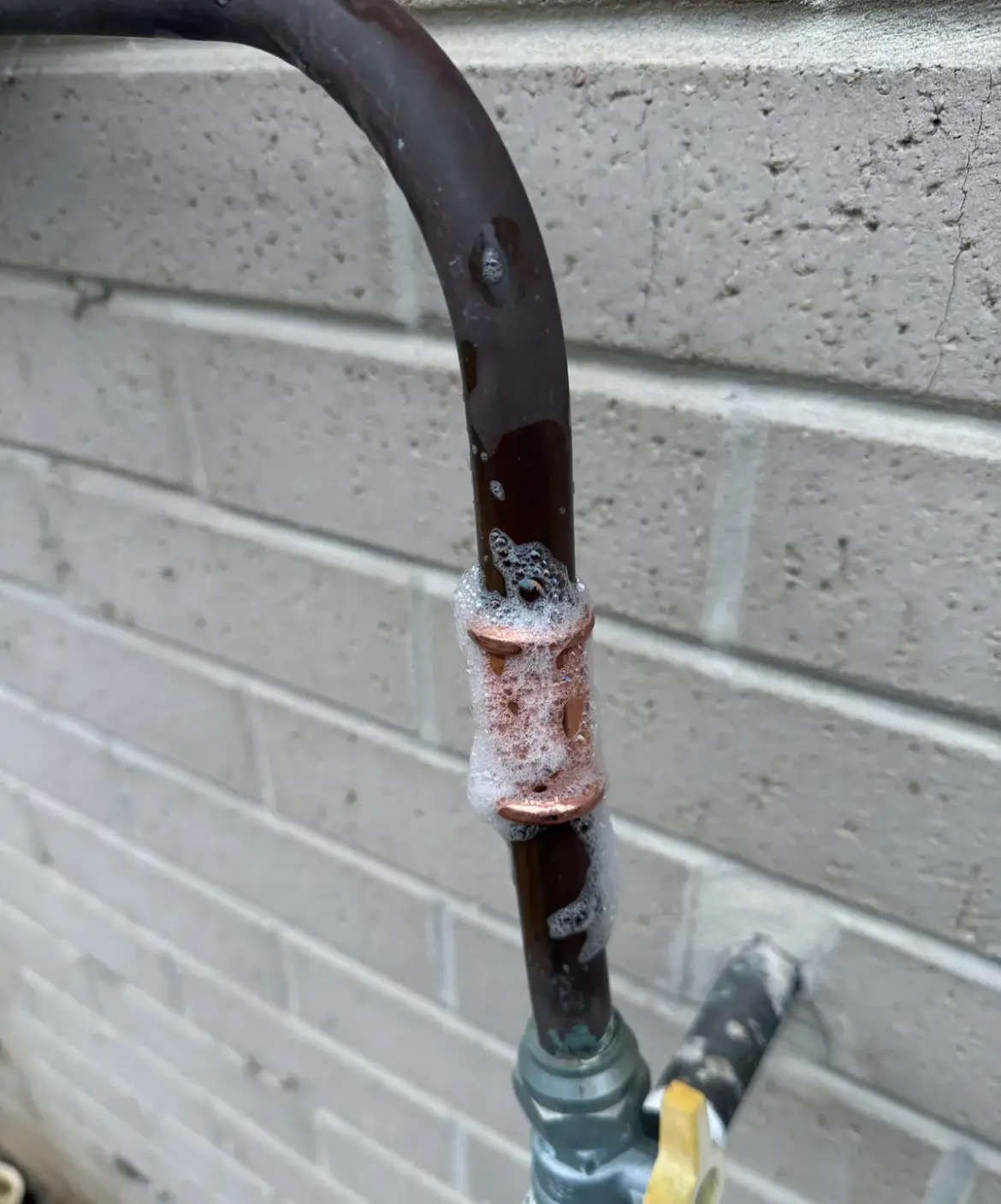 Copper pipe joint covered in leak-test bubbles above a yellow gas valve
