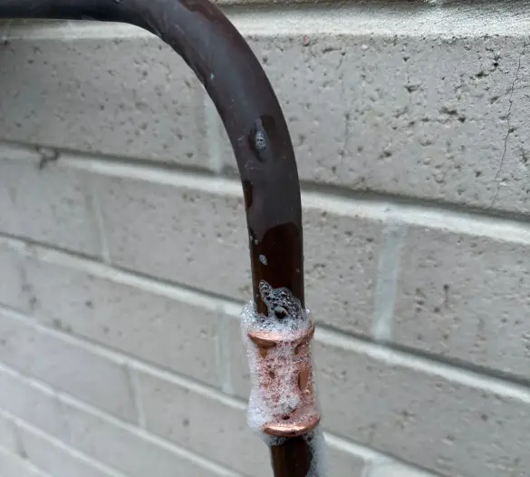 Copper pipe joint covered in leak-test bubbles above a yellow gas valve