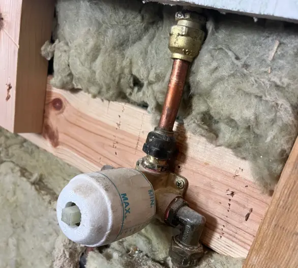 Copper pipework and a tempering valve exposed in a wall cavity between timber studs and insulation