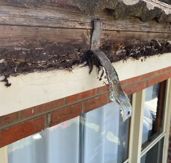 Corroded gutter bracket and rotting timber under the edge of a tiled roof