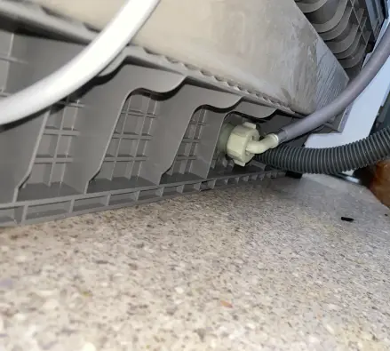Dishwasher base showing the inlet fitting and corrugated drain hose