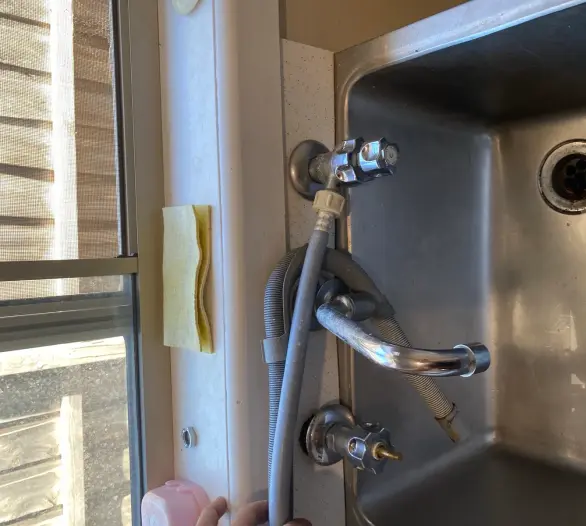 Dishwasher hoses and valves connected beside a stainless steel sink