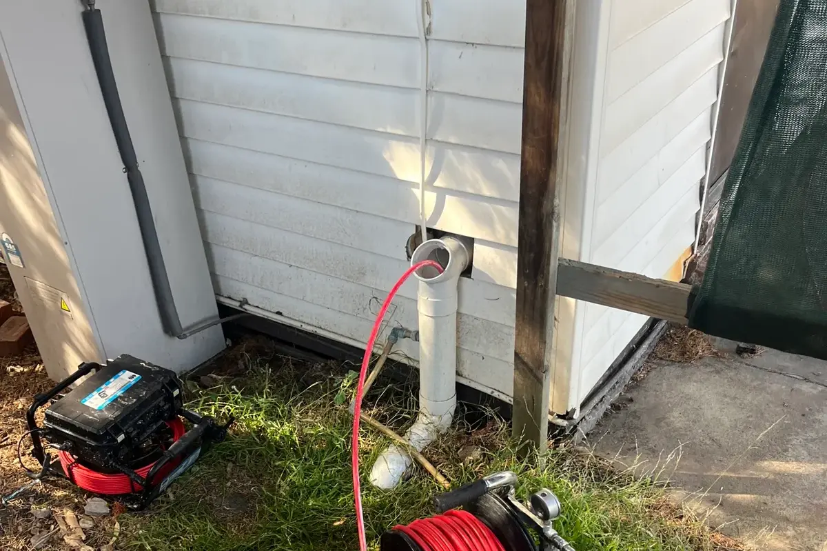 Drain camera and jetter reels laid out beside a house wall under a tarp