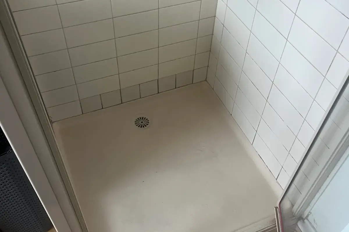 Empty tiled shower recess with a floor drain and a glass door