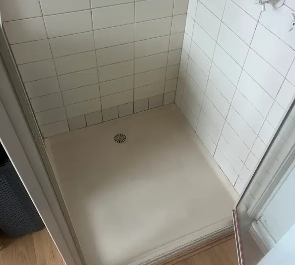 Empty tiled shower recess with a floor drain and a glass door