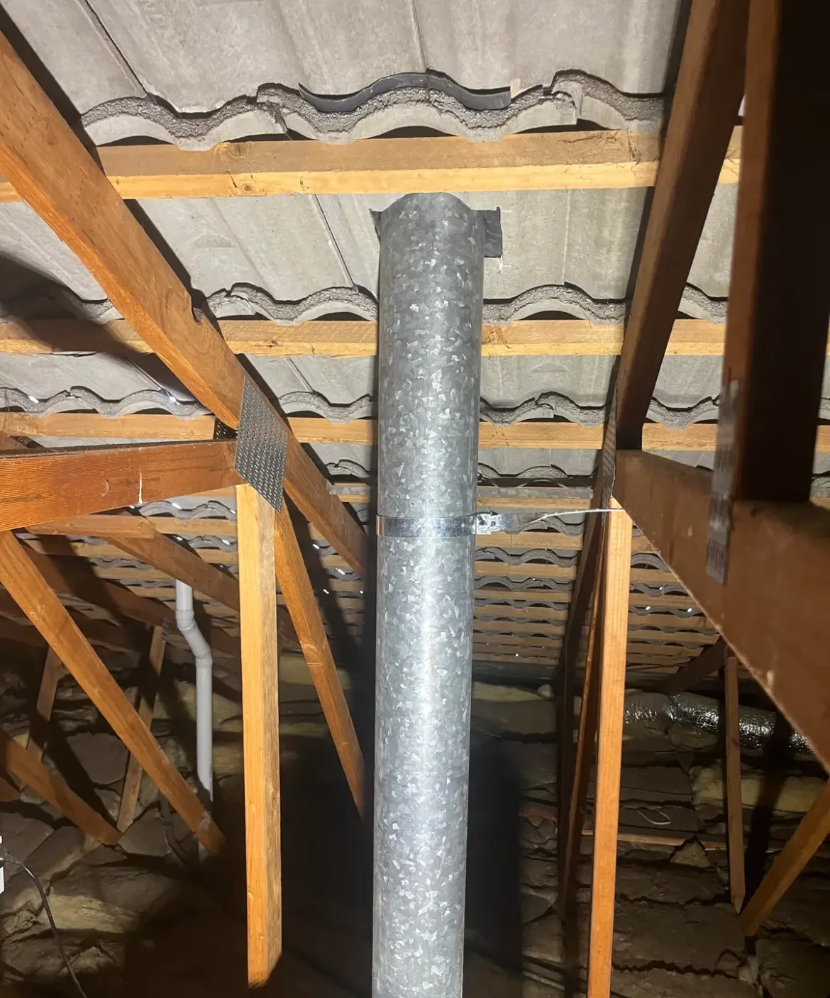 Galvanised flue pipe running up through tiles in a roof space