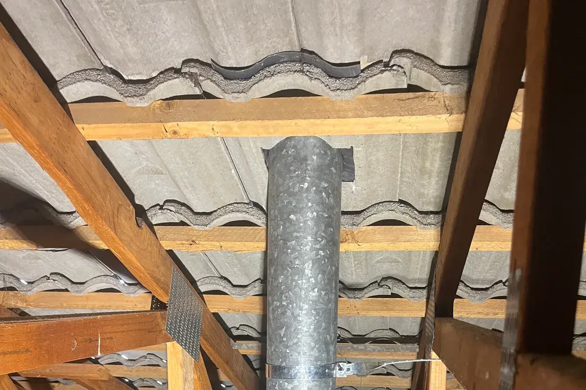 Galvanised flue pipe running up through tiles in a roof space