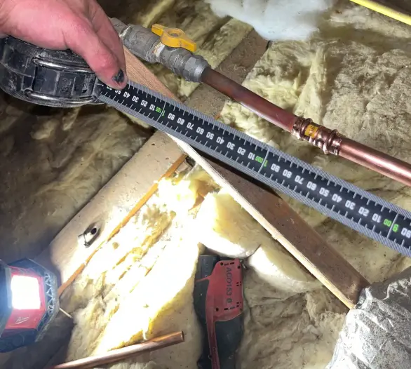 Gas ball valve and copper pipe in a roof space with a measuring tape and a gloved hand
