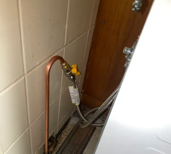 Gas bayonet fitting and braided hose on a tiled wall behind an appliance space