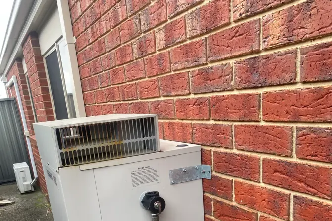Gas hot water unit with a relief valve and pipework against a brick wall