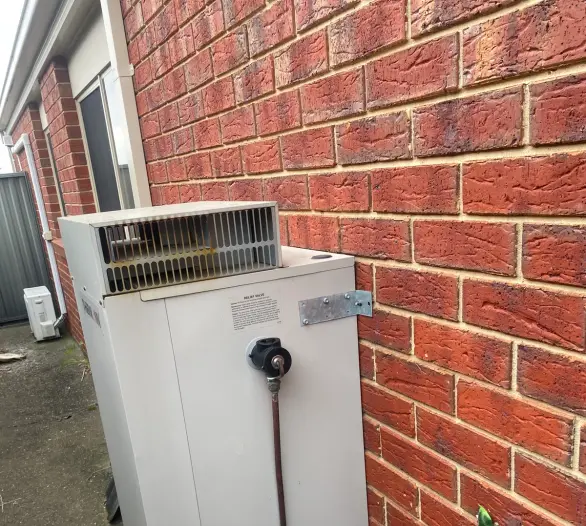 Gas hot water unit with a relief valve and pipework against a brick wall