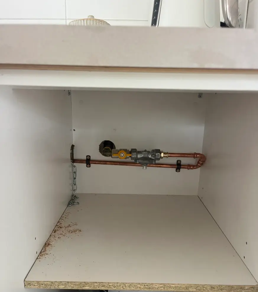 Gas isolator valve and copper pipe in a cupboard under a bench
