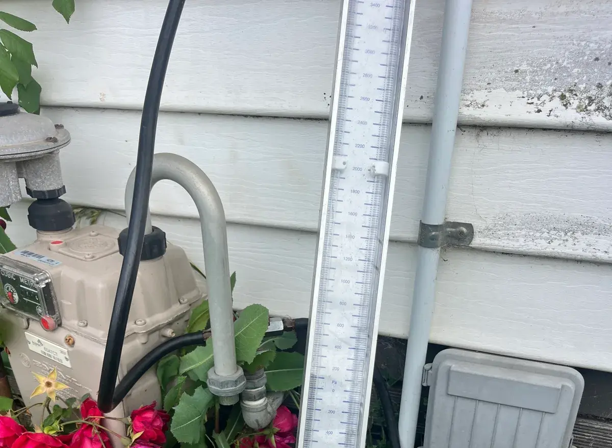 Gas manometer beside a meter on a weatherboard wall with rose bushes