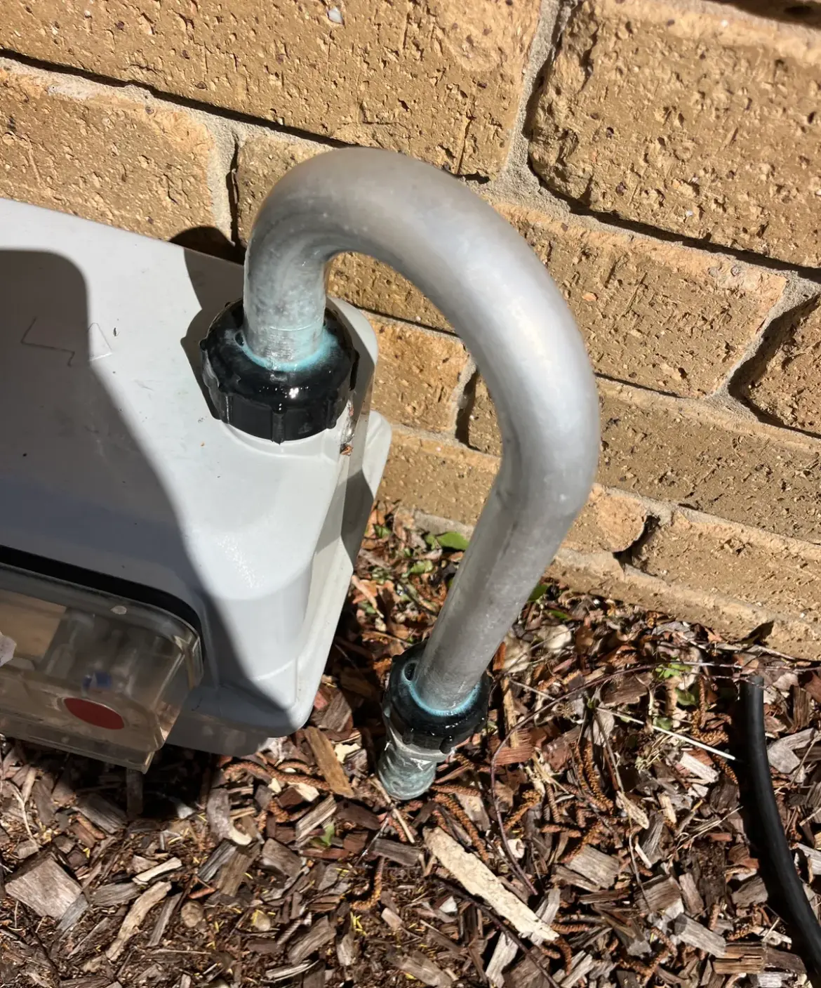 Gas meter and galvanised pipe on a brick wall above garden mulch