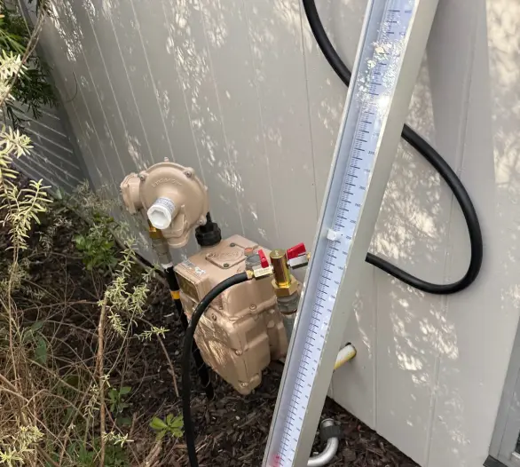 Gas meter and regulator beside plants with a pressure manometer leaning on the wall