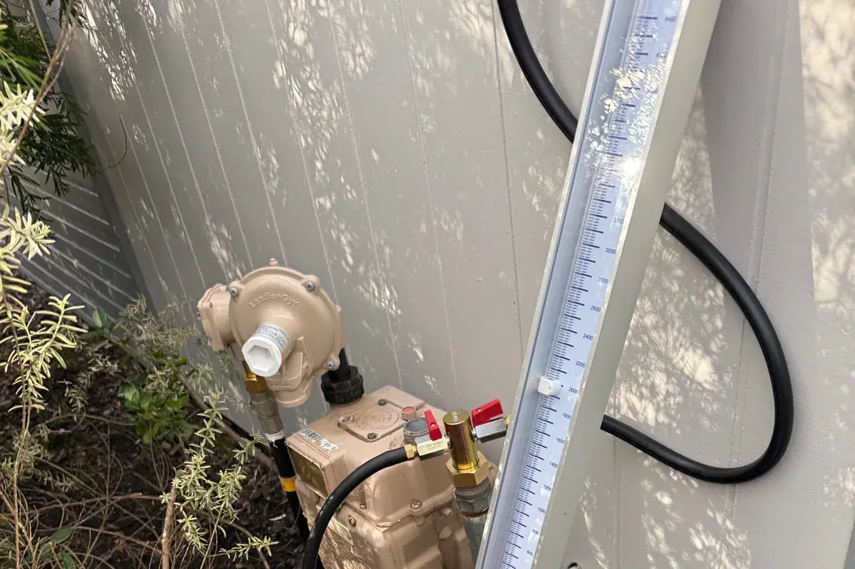 Gas meter and regulator beside plants with a pressure manometer leaning on the wall