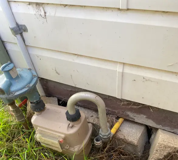 Gas meter mounted on a weatherboard wall with a work boot at the corner