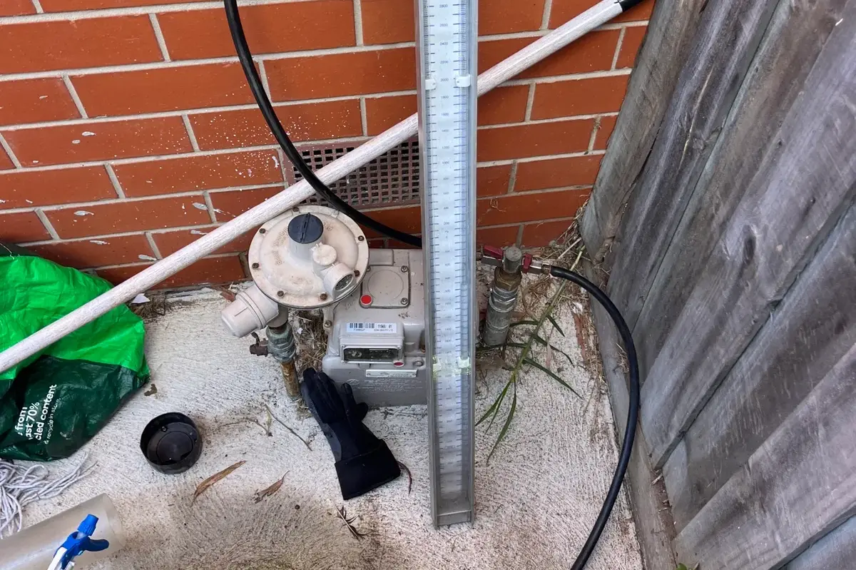 Gas pressure manometer connected at a gas meter beside a brick wall and fence
