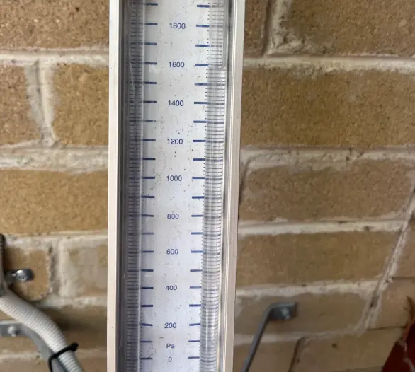 Gas pressure manometer with a scale in pascals held against a brick wall