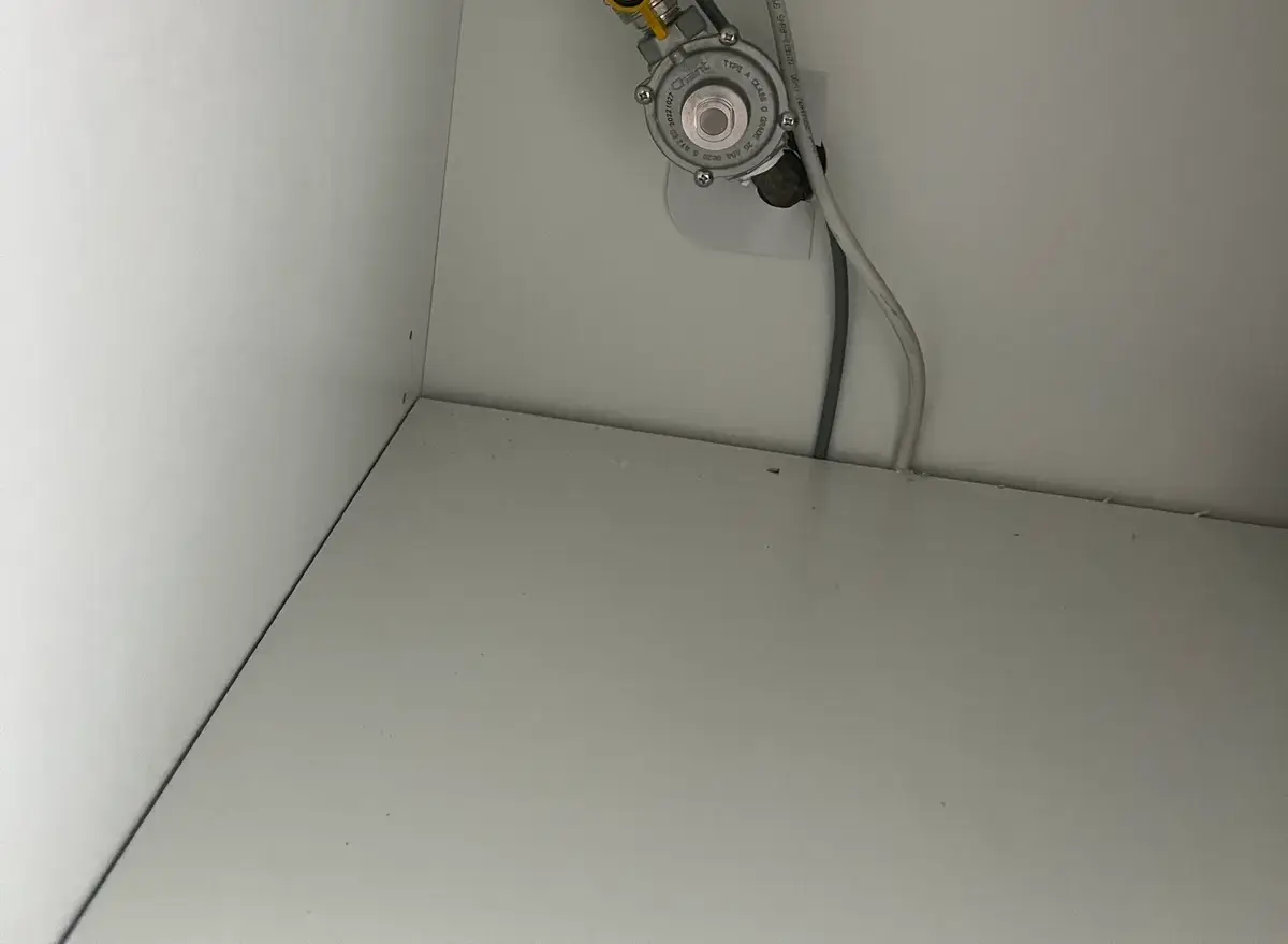 Gas regulator and yellow ball valve fixed inside an empty white cabinet