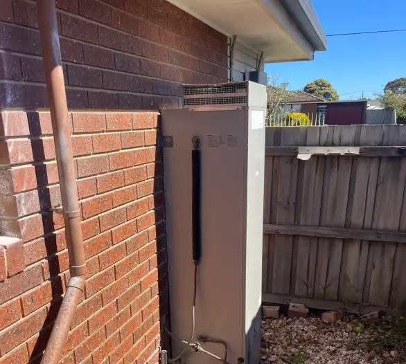 Gas storage hot water unit against a red brick wall beside a fence and pavers