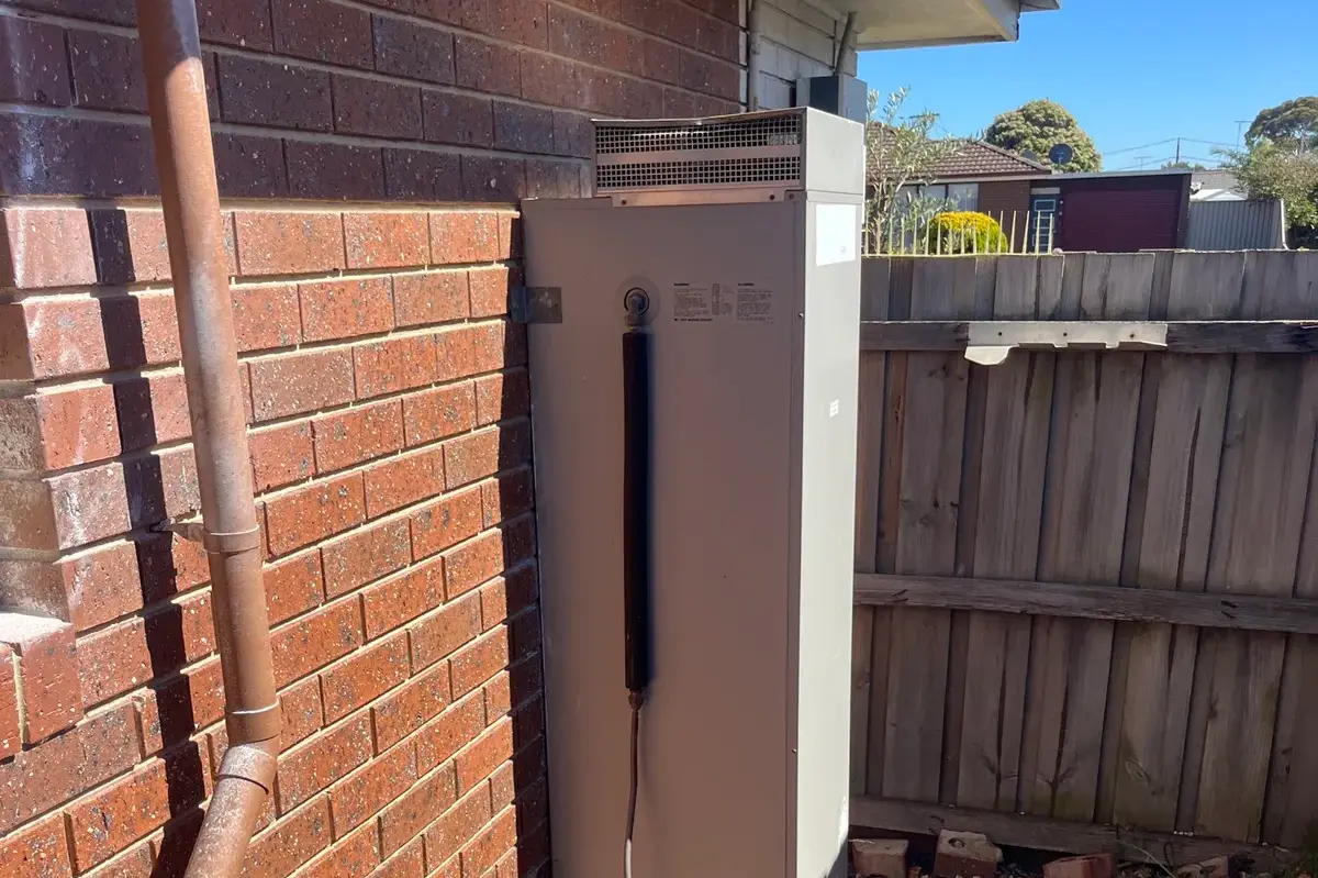 Gas storage hot water unit against a red brick wall beside a fence and pavers