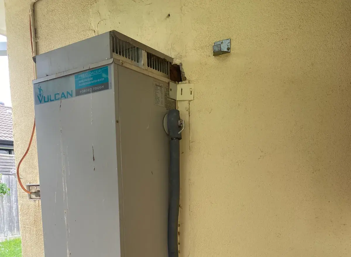 Gas storage hot water unit against a rendered wall beside a barrel