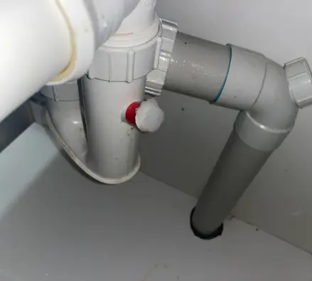Grey and white PVC waste pipework under a sink with a red capped fitting