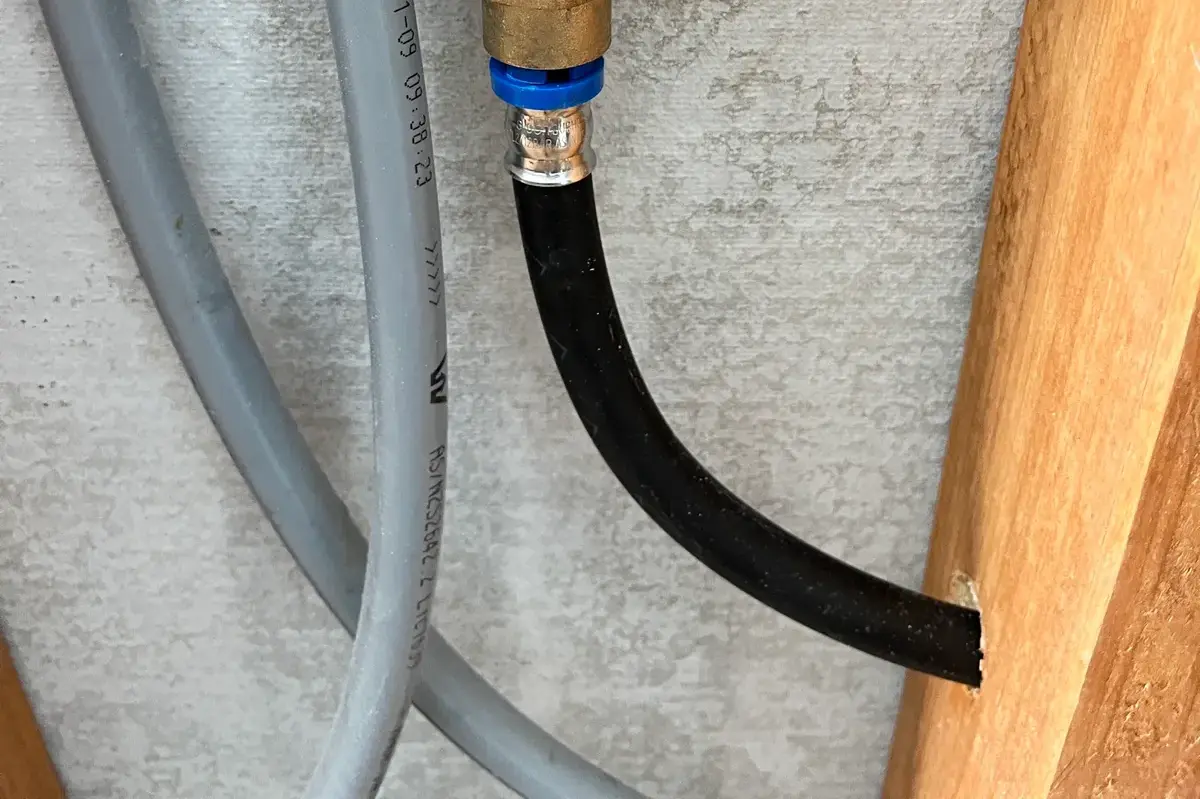 Grey plastic pipe with a brass compression fitting and black hose fixed to a wall